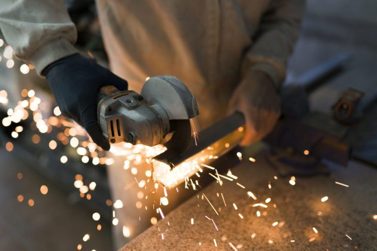 Professional bricklayer cutting an iron bar with a cutter while releasing large colored sparks